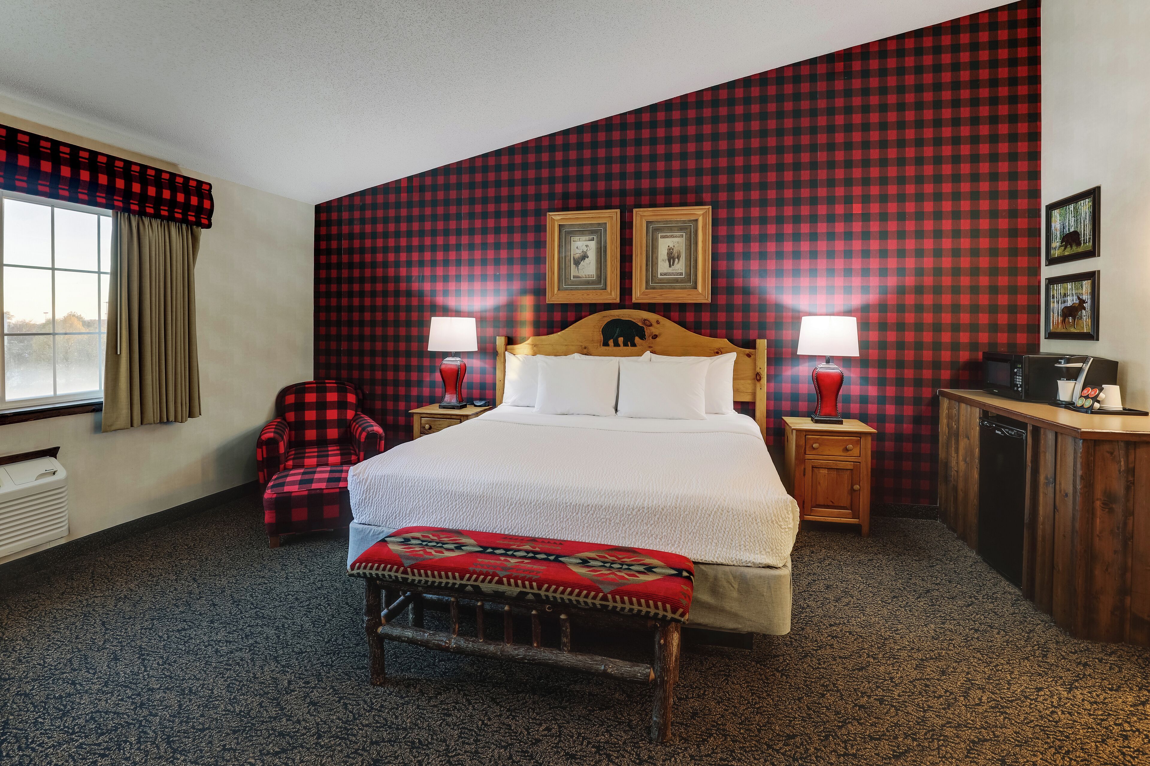 Ein Hotelzimmer mit einem großen Bett, zwei Nachttischen mit Lampen, einer hölzernen Bank, einem roten karierten Sessel und einer karierten Wand.