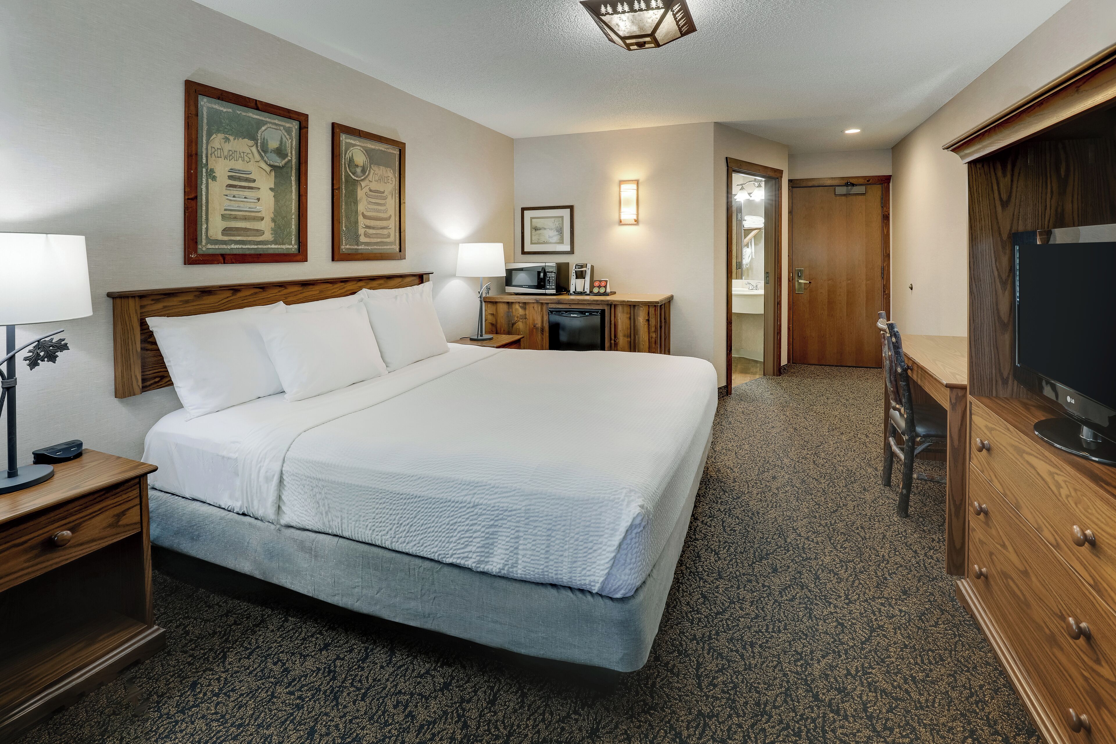 A hotel room with a large bed, a desk with a lamp, a microwave, and a television.