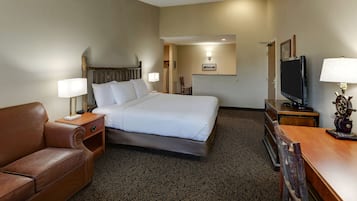 A hotel room with a bed, a brown leather sofa, a wooden desk with a lamp, and a television.