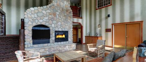 A stone fireplace with a TV, wooden furniture, and a staircase leading to an upper level.
