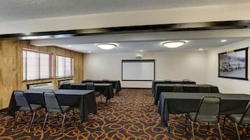 A conference room with tables and chairs, a projector screen, and a carpeted floor.