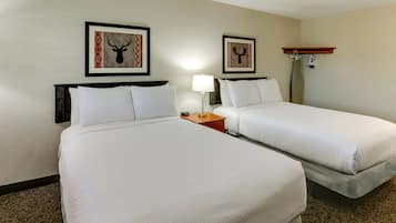 Habitación de hotel con dos camas, una mesita de noche con una lámpara y dos cuadros con la imagen de ciervos montados en la pared.