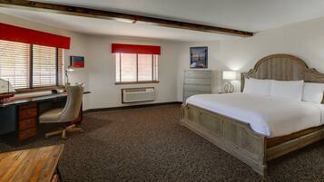 Quarto de hotel com uma cama de madeira, uma escrivaninha com cadeira, um aparador e um radiador.