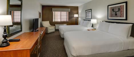 A hotel room with two beds, a desk, a chair, a mirror, and a framed picture on the wall.