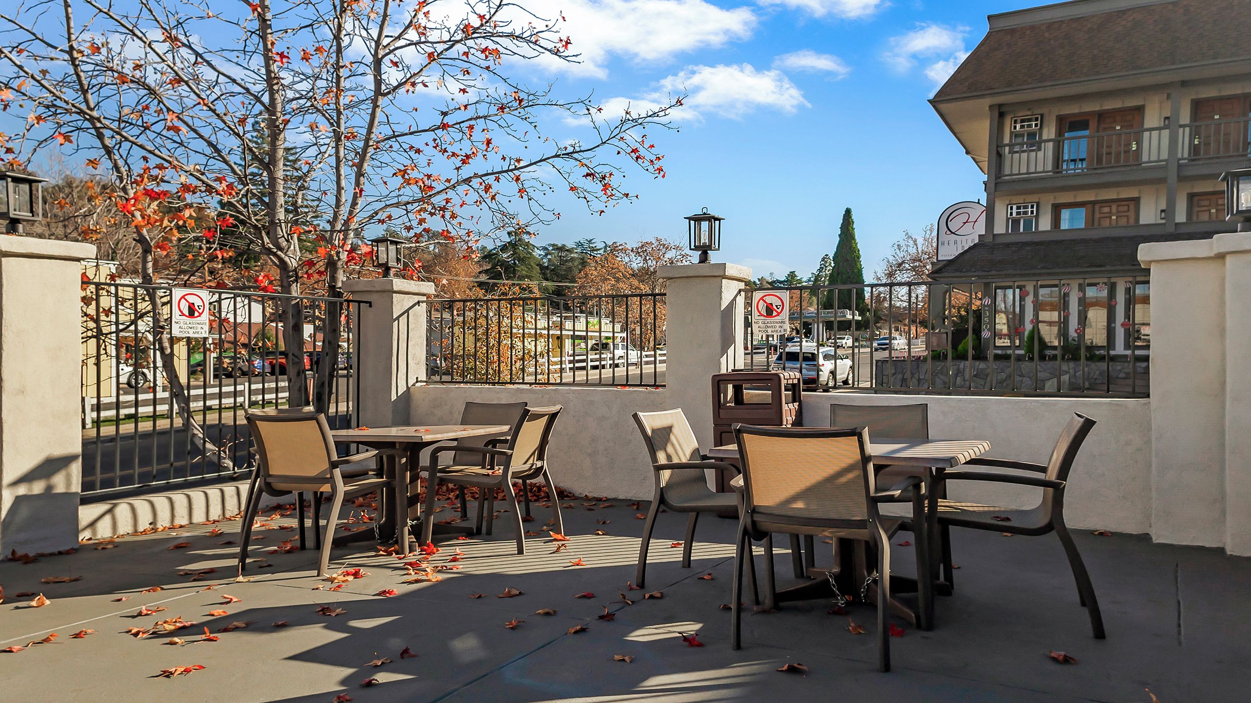 An outdoor patio with tables and chairs, a view of the street, and a building in the background.