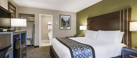 A hotel room with a bed, bedside tables, a desk with a TV, a mirror, and a bathroom visible through an open door.