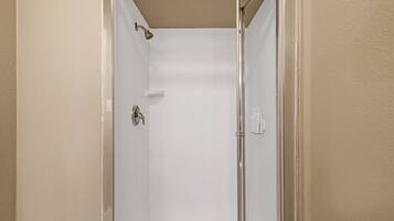 Cabina de ducha con paredes de vidrio, cabezal de ducha, perchero y dispensador de jabón.