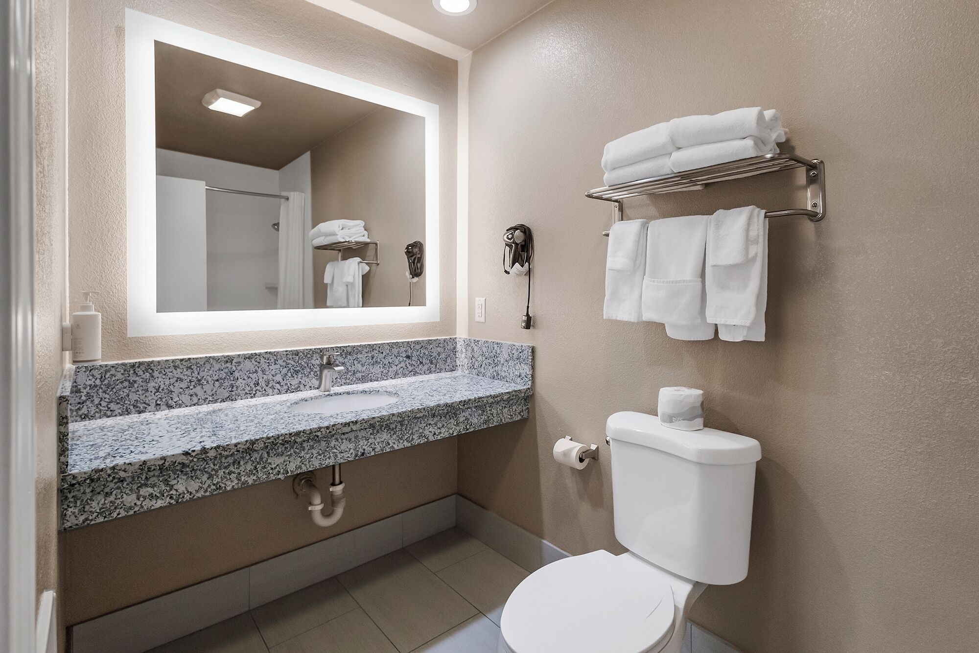 A modern bathroom with a granite countertop sink, a toilet, a towel rack, and a mirror.