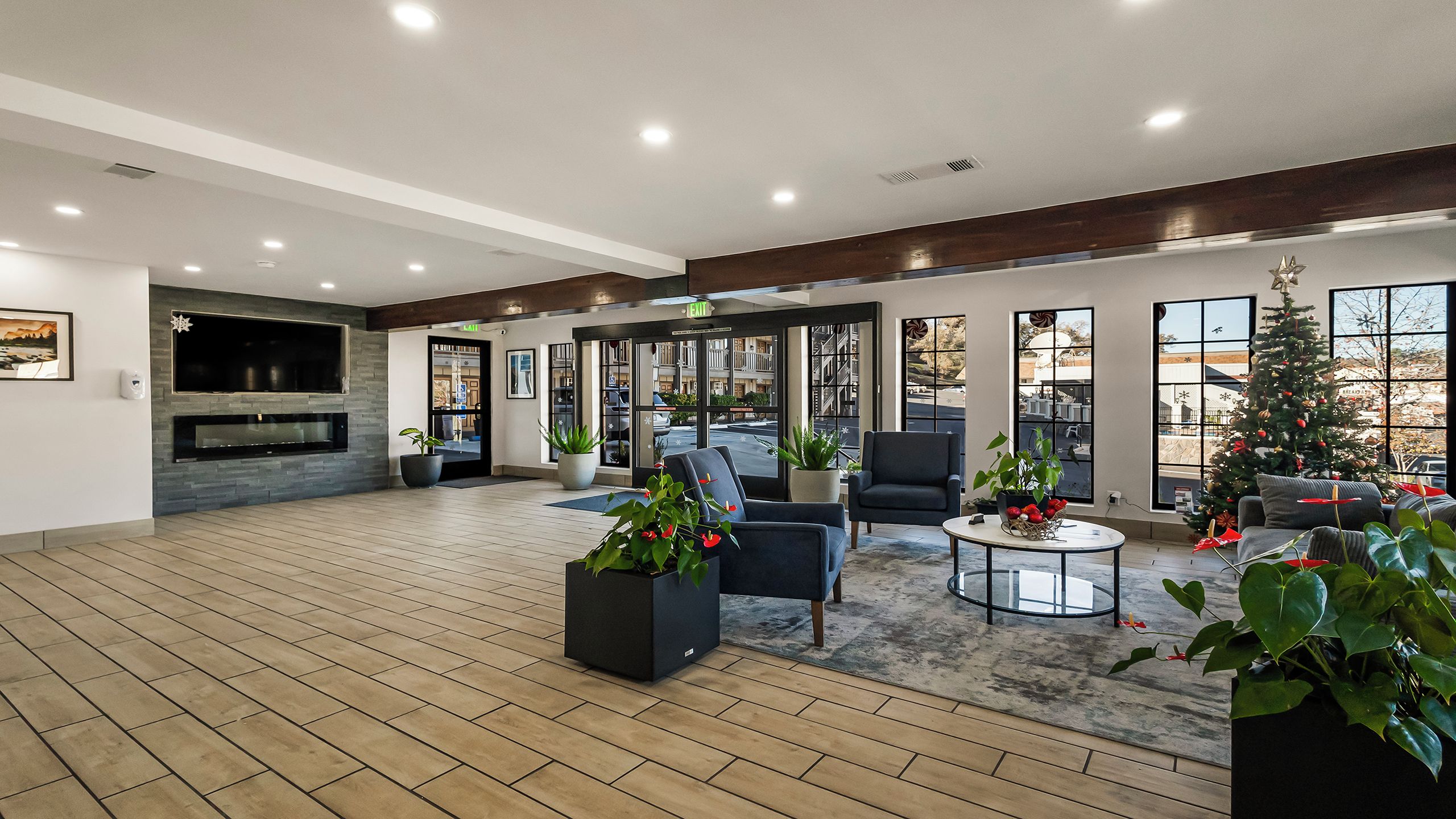 A spacious living area with a fireplace, comfortable seating, large windows, and a Christmas tree.