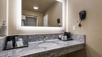 A bathroom with a granite countertop, a sink, a mirror, a hairdryer, and a towel rack.