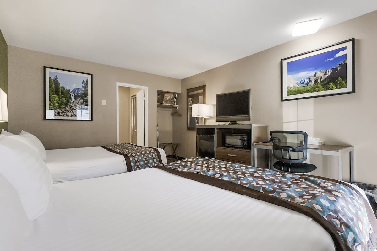 A hotel room with two beds, a desk with a computer, a TV, and a microwave.