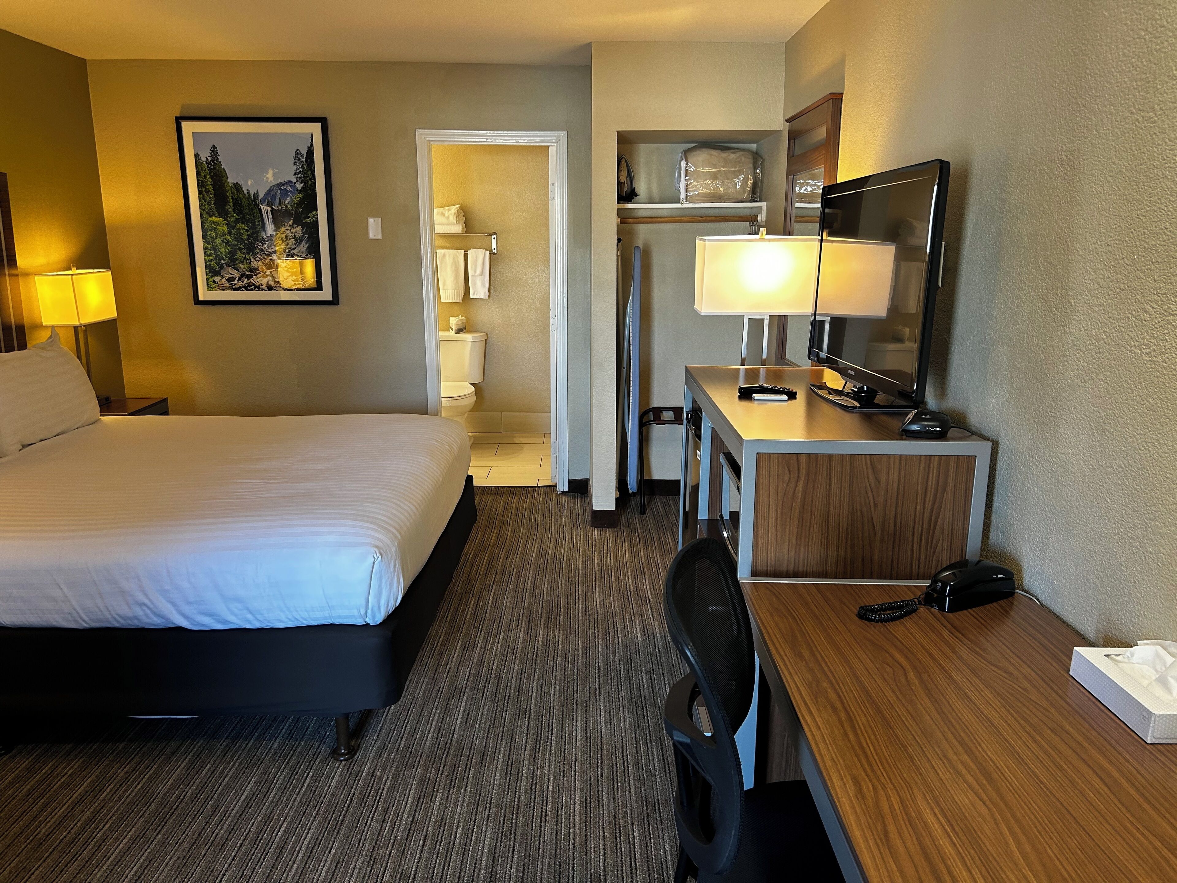 A hotel room with a bed, desk, chair, desk lamp, and a television.