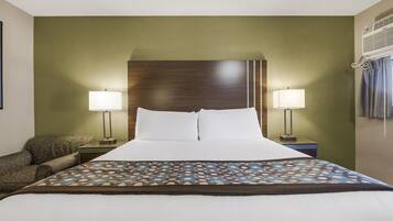 Een hotelkamer met een groot bed, twee bedlampjes, een bedspread met een patroon en een houten hoofdbord.