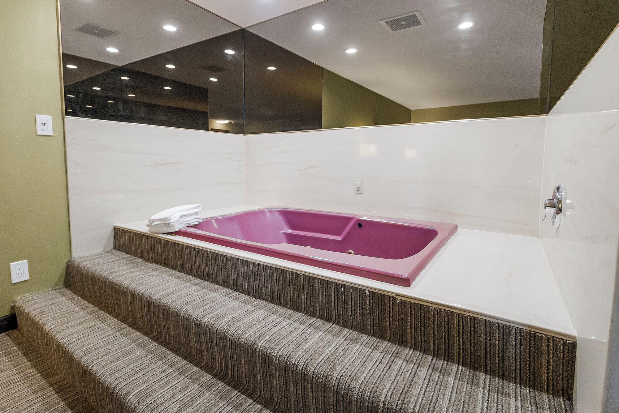 Une salle de bain moderne avec une grande baignoire rose, un miroir et un petit escalier menant à la baignoire.