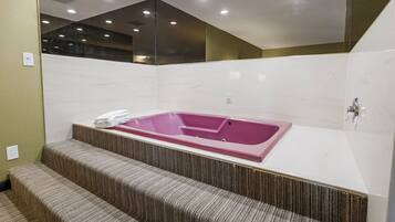 Une salle de bain moderne avec une grande baignoire rose, un miroir et un petit escalier menant à la baignoire.