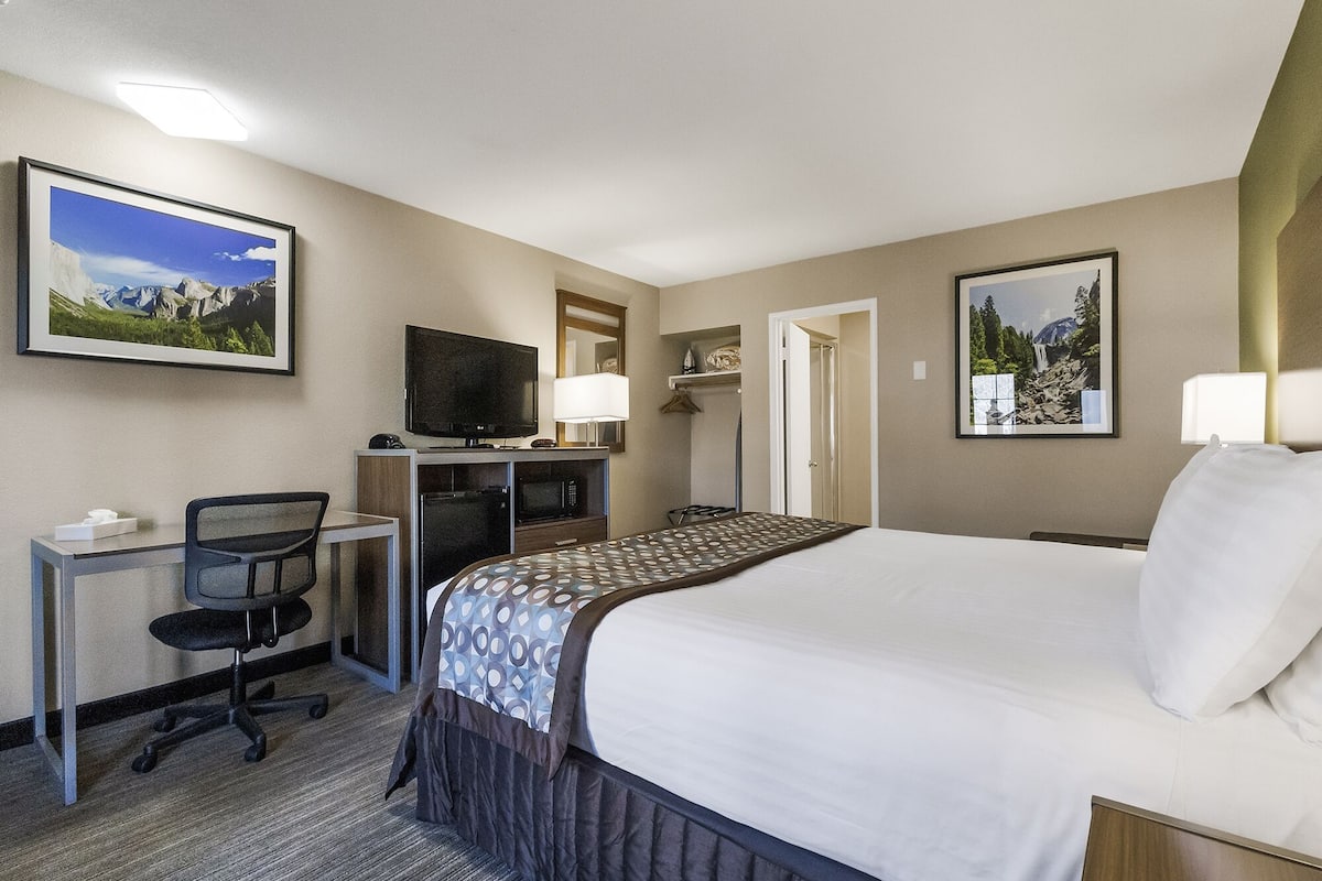 A hotel room with a bed, a desk with a computer, a TV, and two framed pictures on the wall.
