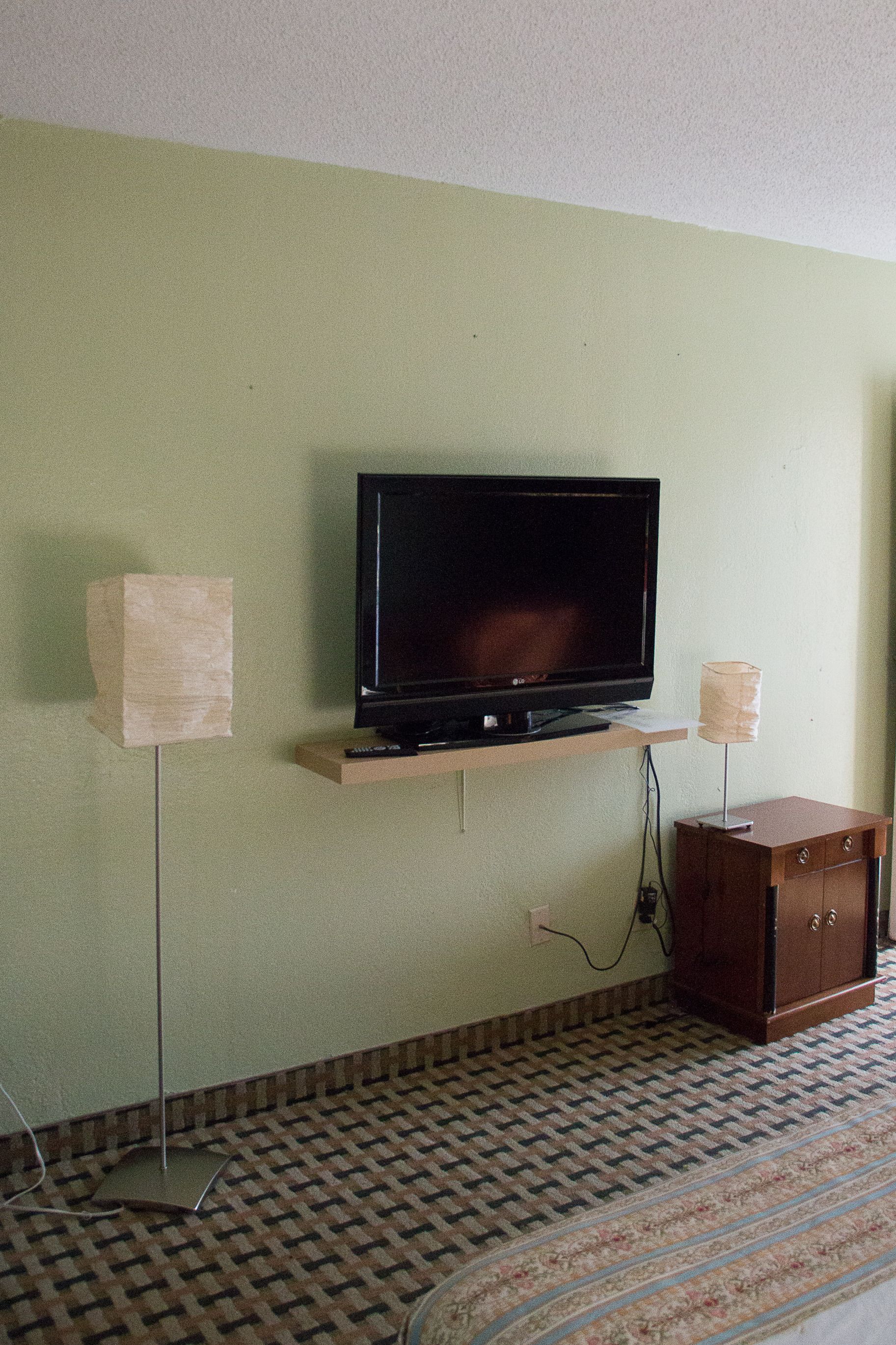A television on a stand against a wall, a small cabinet below it, and a patterned carpet.