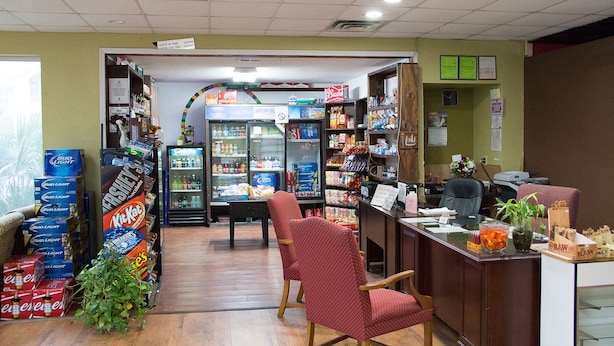 A small convenience store with a variety of products including snacks, beverages, and candy. There is a refrigerator, a counter with a cash register, and a few chairs. - Cocomo Inn and Suites (Moultrie)