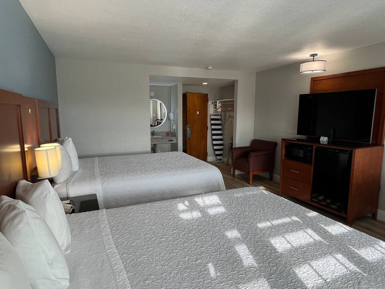 A hotel room with two beds, a desk, a TV, and a bathroom visible through an open door.
