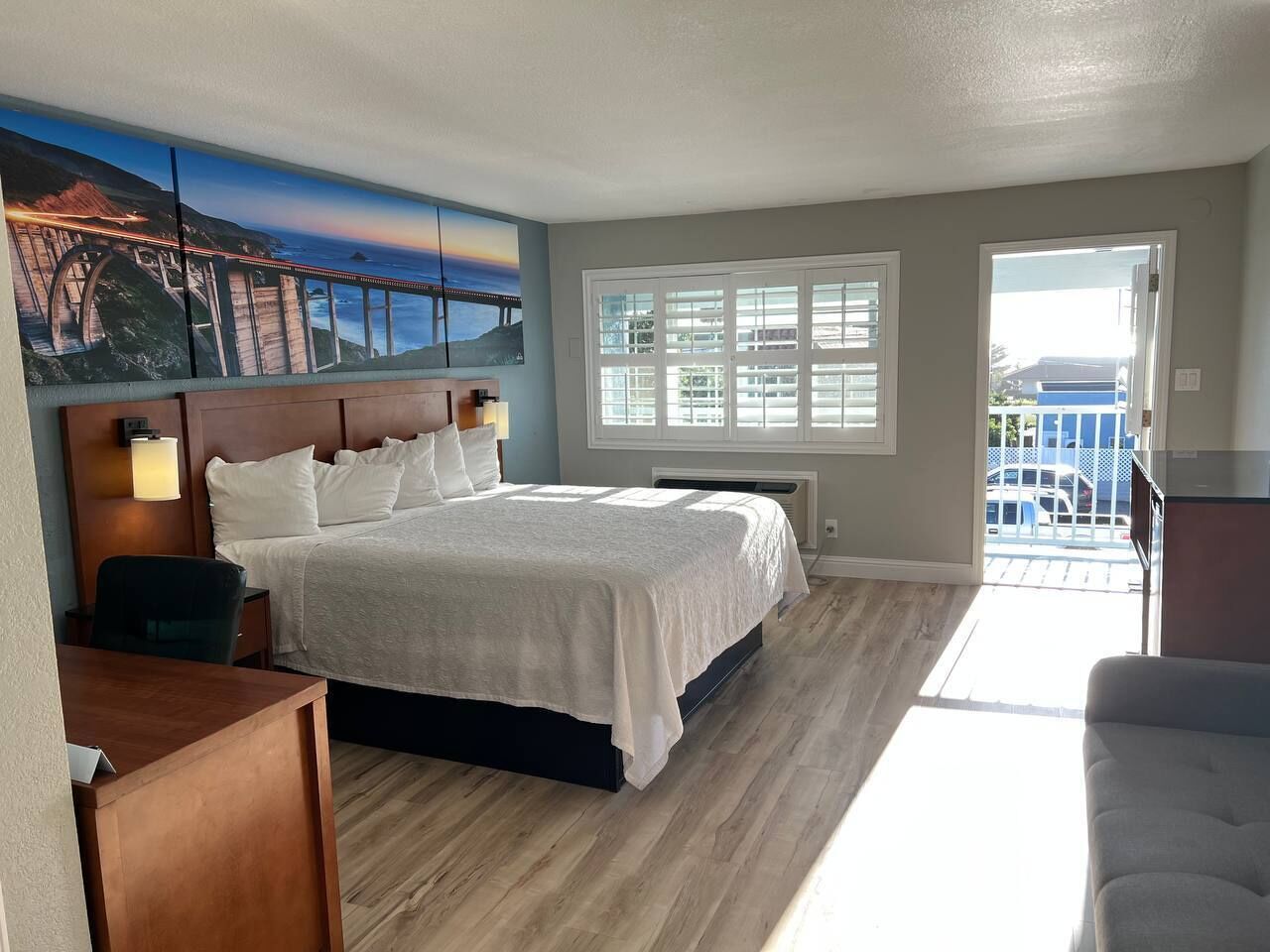 A hotel room with a large bed, a desk, a chair, a window with blinds, and a view of the outside.
