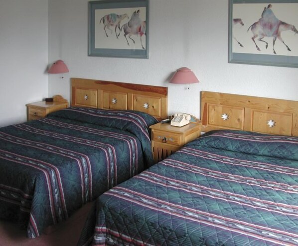 A hotel room with two beds, wooden headboards, a nightstand with a phone, and two wall-mounted lamps. - Sun God Lodge (Taos)