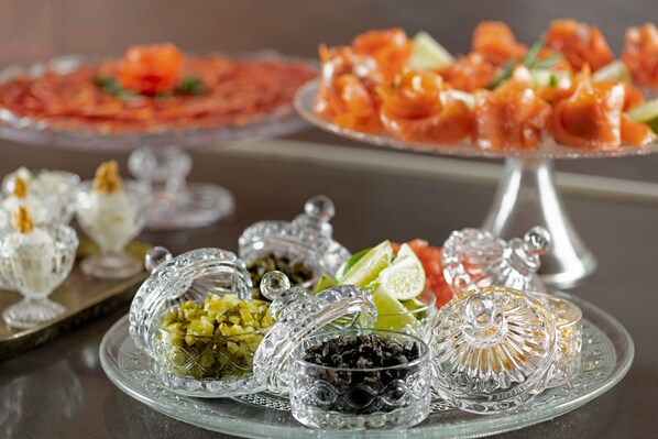Variedad de alimentos sobre una mesa, incluyendo un plato de salmón y otro con aceitunas y alcaparras.
