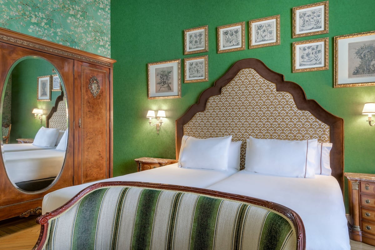 A hotel room with a large bed, a mirror, and a green wall with framed artwork.