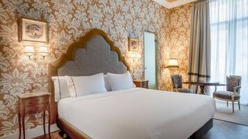 Una habitación de hotel con una cama grande, dos mesitas de noche, una butaca, una pequeña mesa y un espejo.