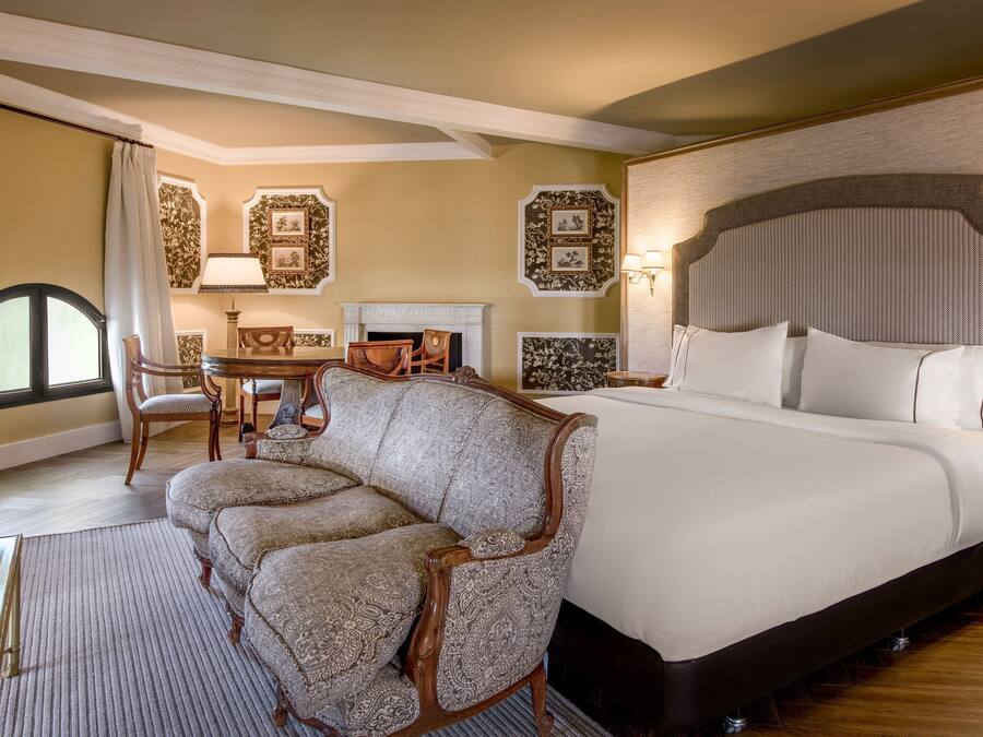 Una habitación de hotel con una cama grande, un sofá, una chimenea y una mesa de comedor.