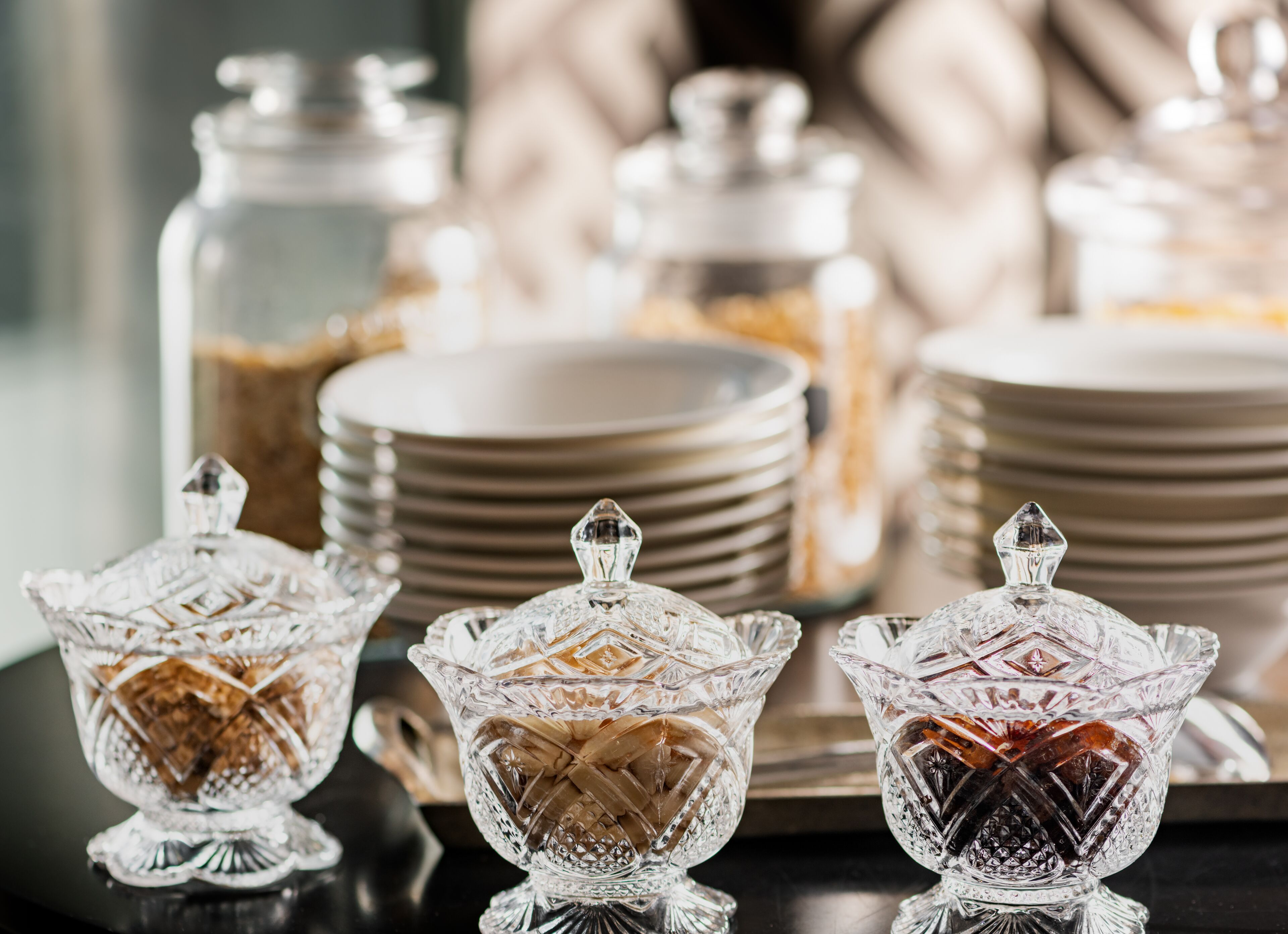 Une table avec trois récipients en verre contenant du sucre brun, une pile d’assiettes et un arrière-plan flou.