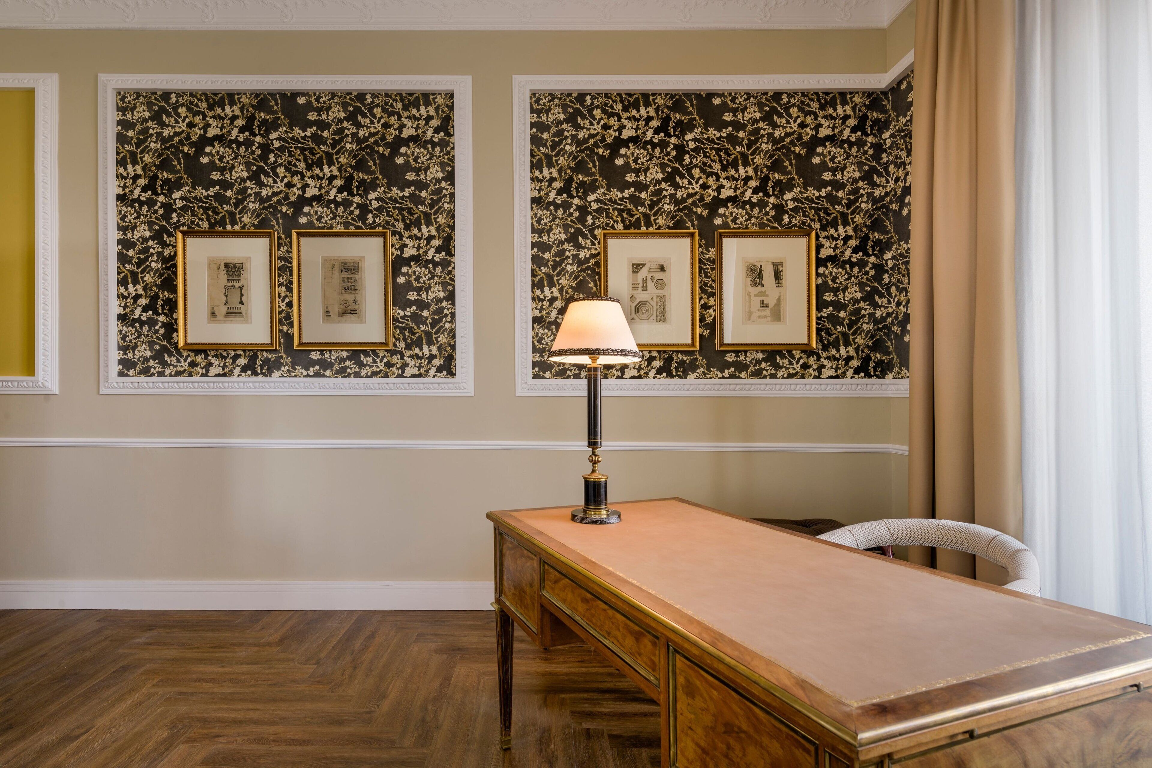 Una habitación con un escritorio de madera, una lámpara, cuadros en la pared y una silla.