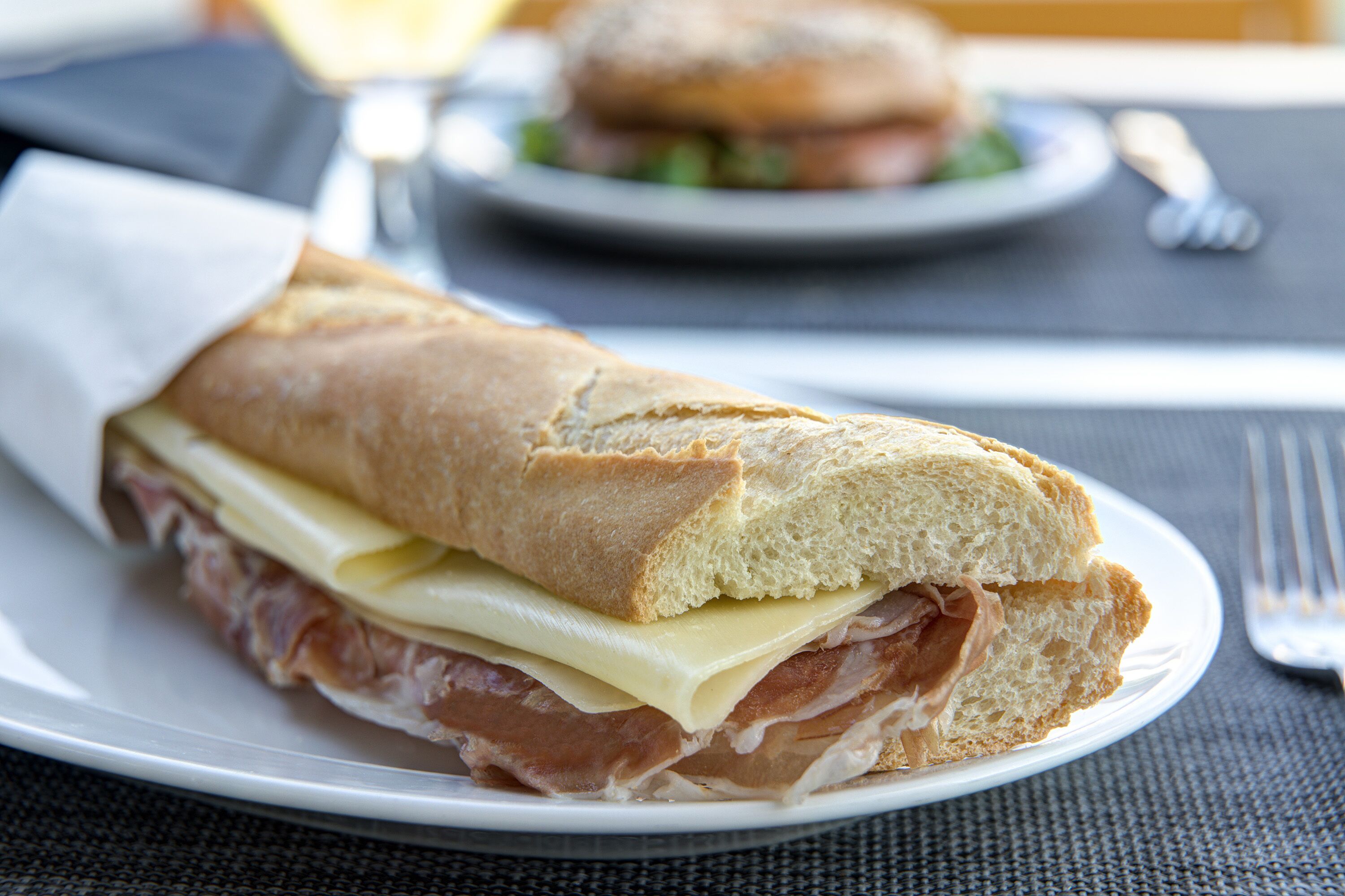Un sándwich en un plato, con un tenedor y un cuchillo cerca.