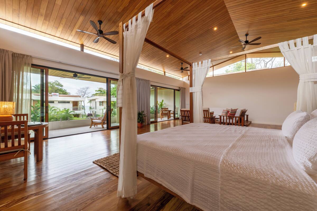 A spacious bedroom with a large bed, wooden ceiling, and ceiling fans.