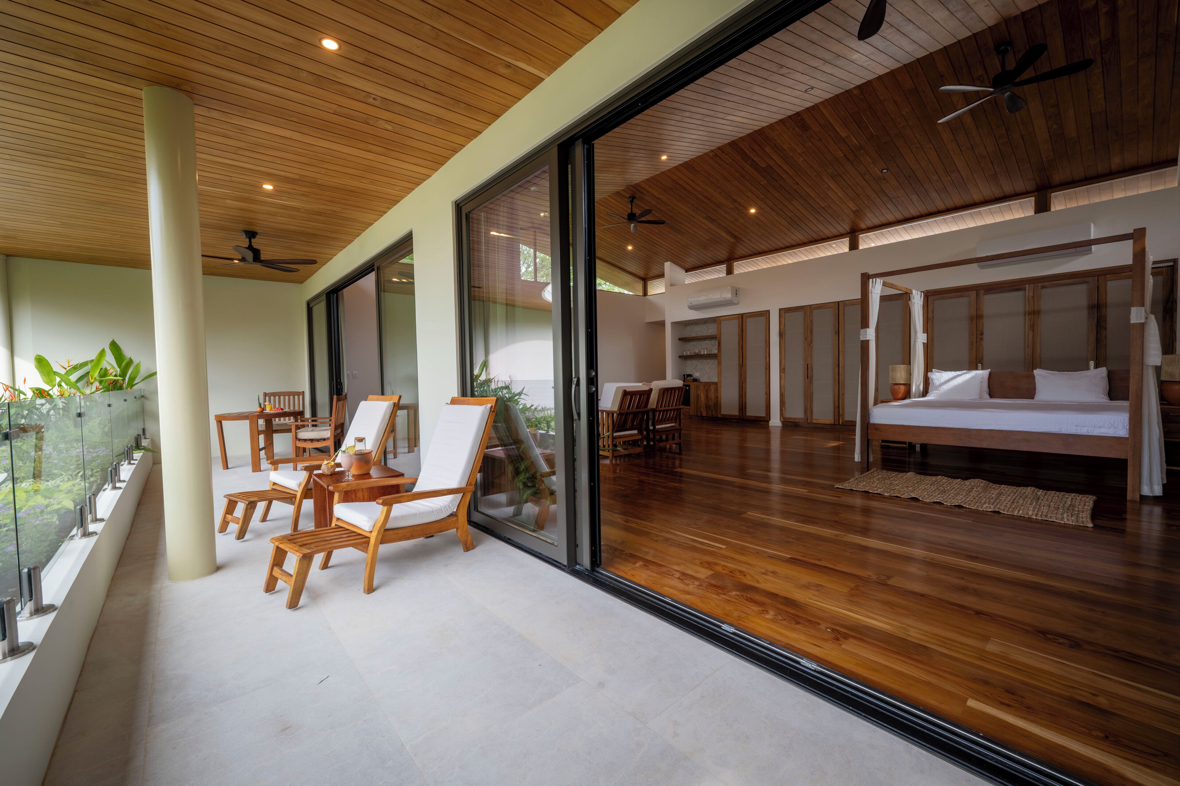 A spacious room with a large bed, wooden flooring, and a balcony with seating.