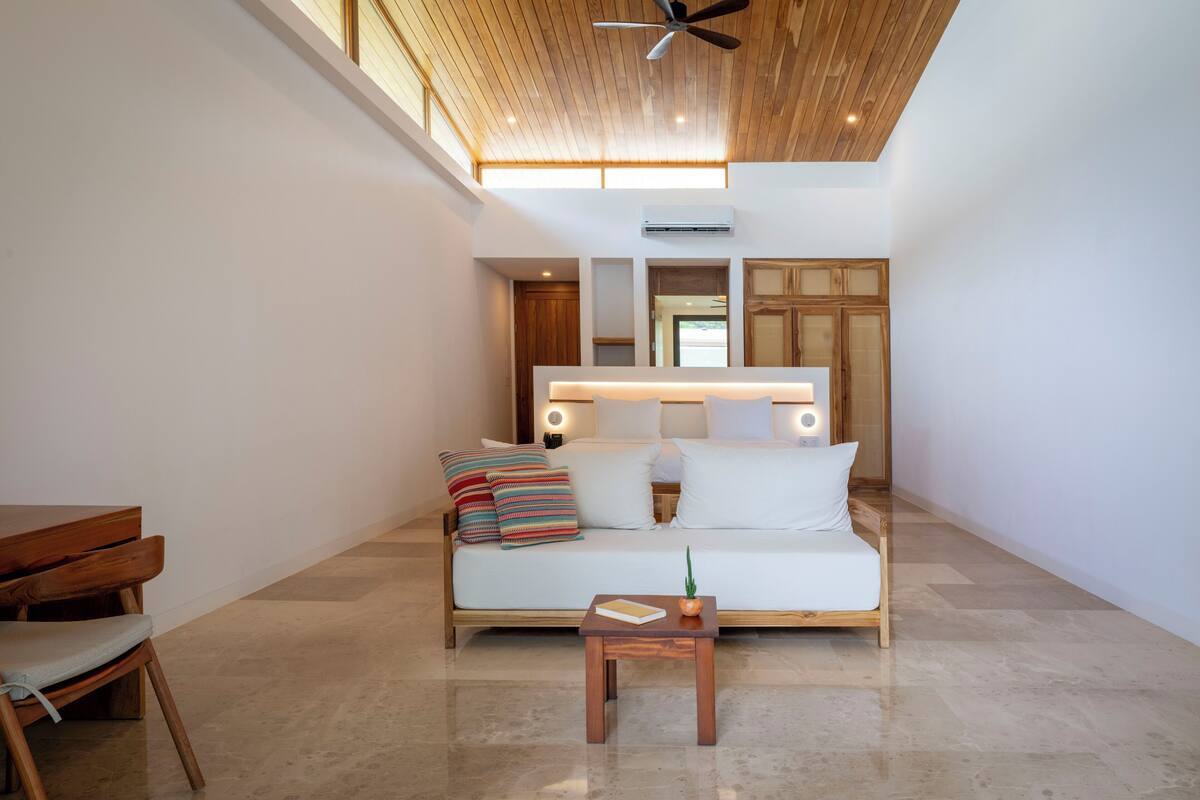 A modern living room with a wooden ceiling, a white sofa with cushions, a small wooden table, and a ceiling fan.