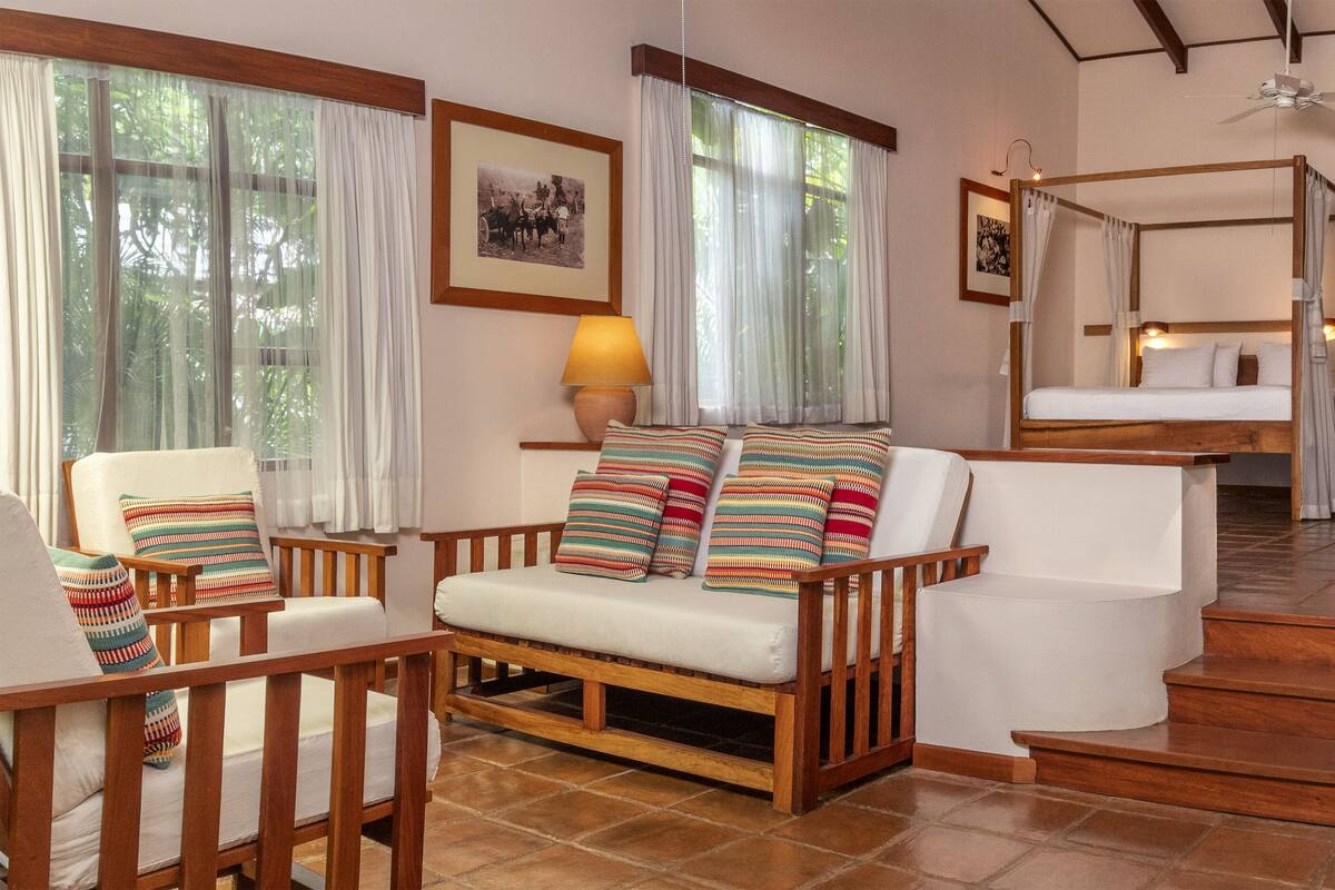 A cozy room with a sofa, a wooden chair, a bed with a canopy, and a staircase.