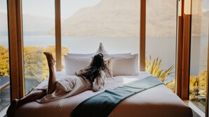 Un dormitorio con un gran ventanal que da a un cuerpo de agua y montañas.