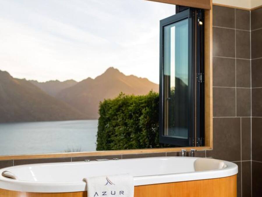 A modern bathroom with a freestanding bathtub, a view of mountains and a lake, and a wooden vanity.