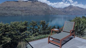 Una terraza con una silla de descanso y una mesa con vista a un lago y montañas al fondo.