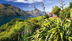 Un paisaje montañoso con un lago, un edificio rojo de diseño moderno y abundante vegetación.