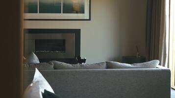 A modern hotel room with a large bed, a sofa, a fireplace, and a ceiling fan.