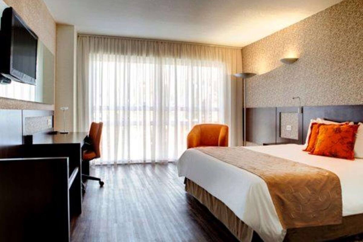 A hotel room with a large bed, a desk, a chair, and a television.