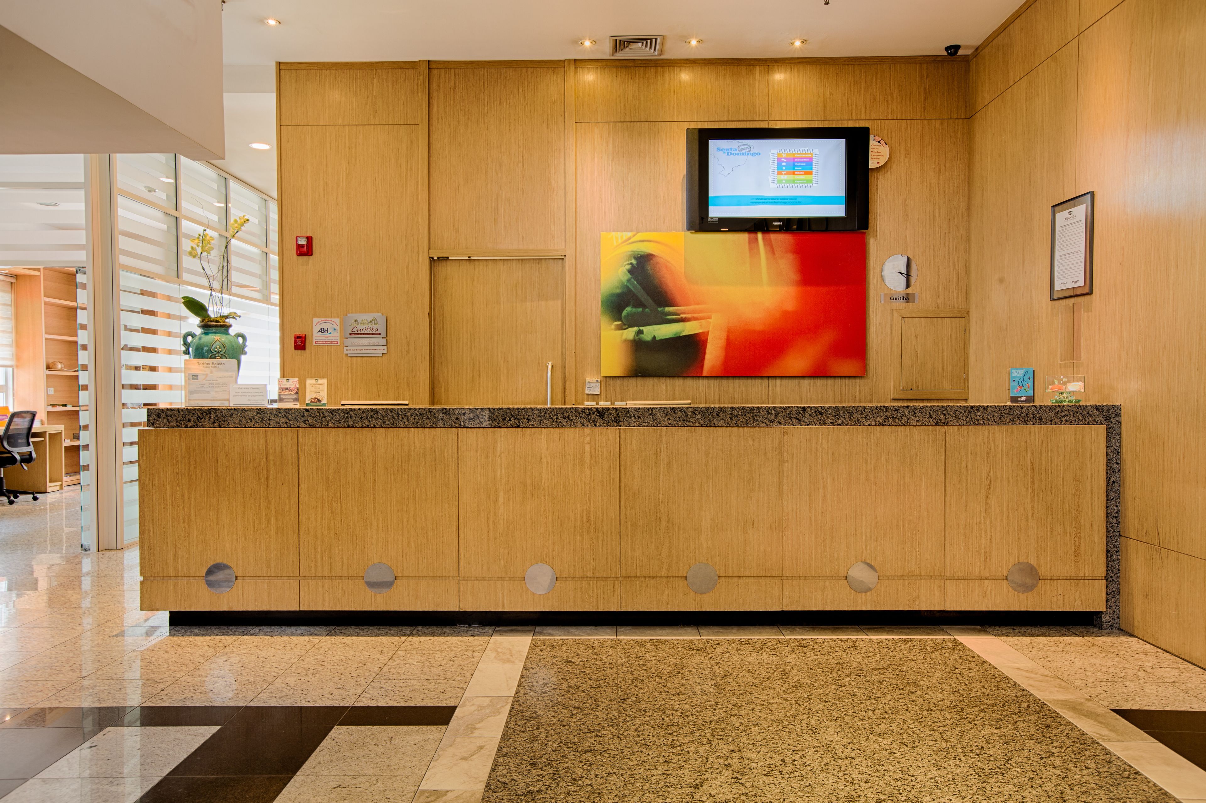 A reception desk with a flat-screen TV, a clock, and a vase with flowers.