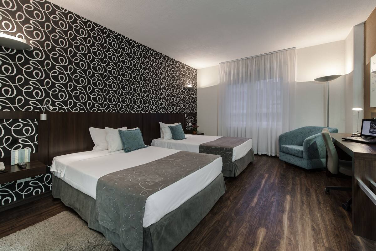 A hotel room with two beds, a desk, a chair, and a large mirror.