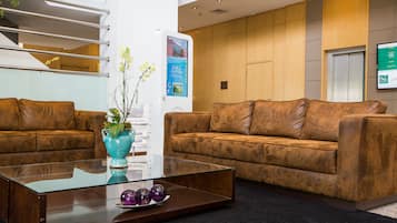 Um hall moderno com dois sofás de couro marrom, uma mesa de centro de vidro e um vaso azul-turquesa com flores.