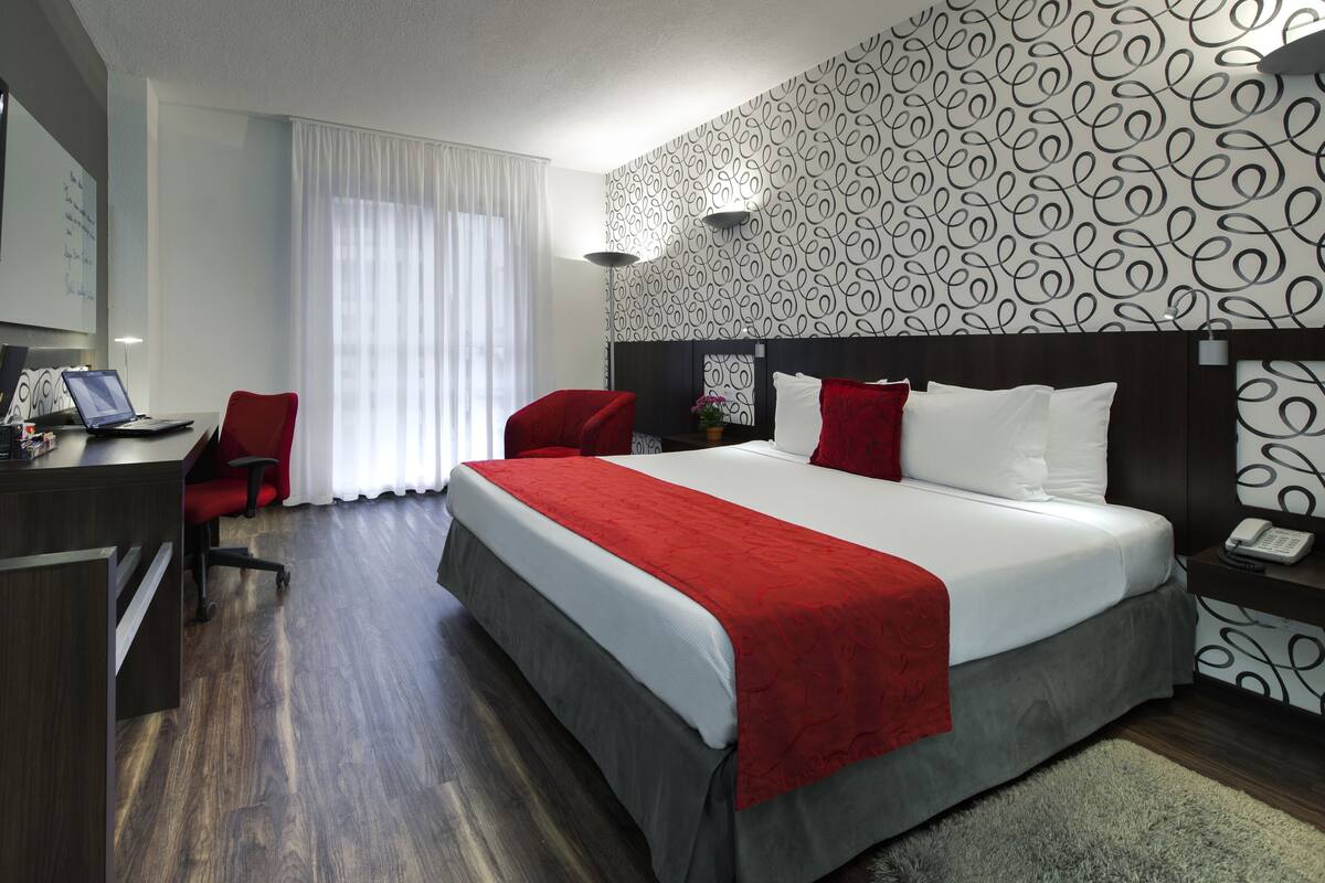A hotel room with a bed, desk, chair, and a TV.