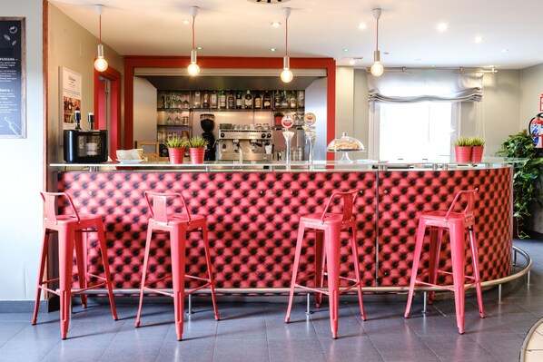 Una zona de bar con un mostrador de diseño rojo y negro, taburetes rojos y una máquina de café.