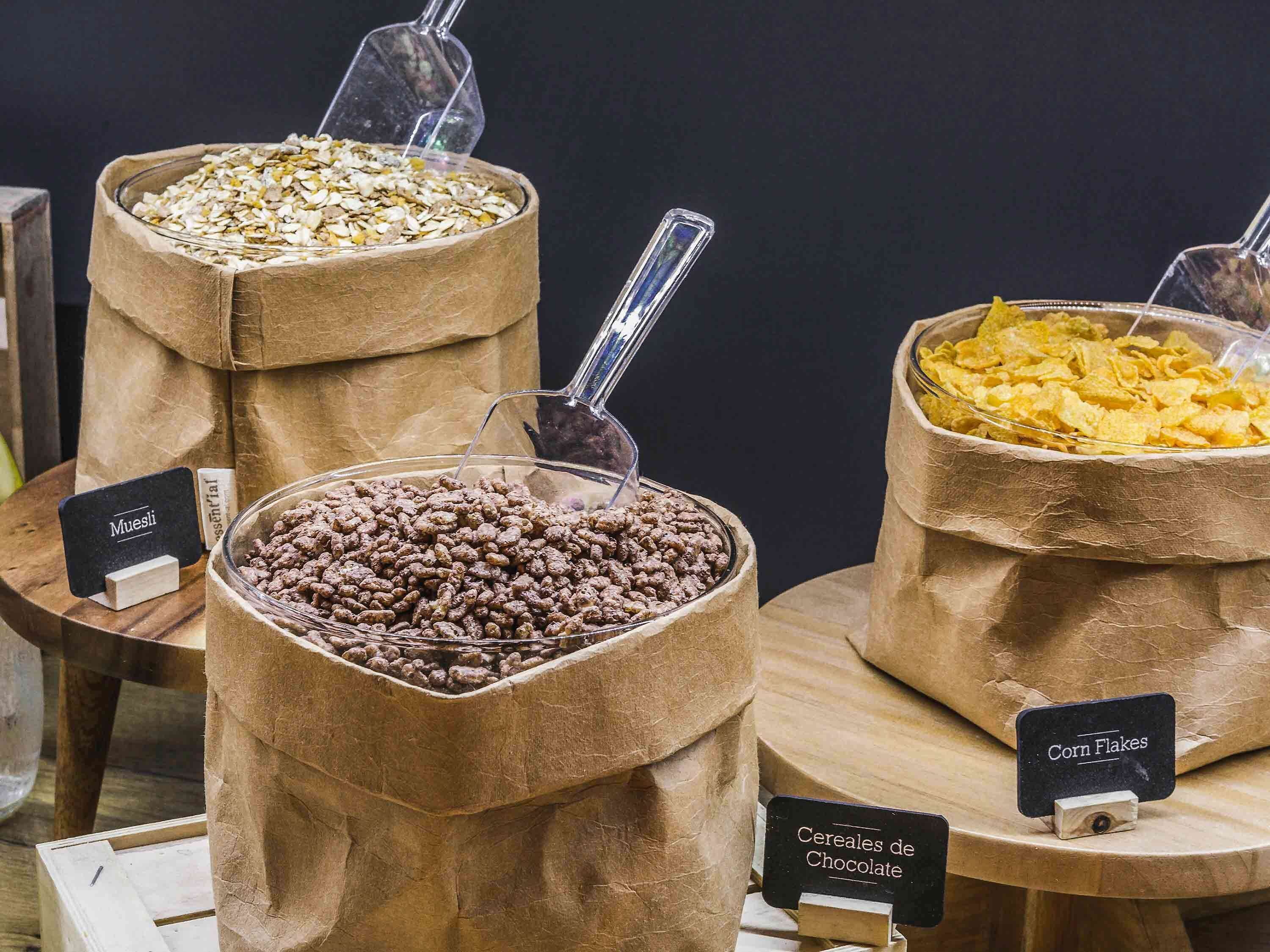 Tres recipientes etiquetados con diferentes alimentos: Muesli, Cereales de Chocolate y copos de maíz.