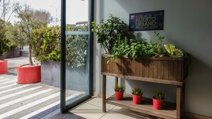 Un área de recepción con un banco de madera con plantas en macetas, puerta de vidrio de entrada y un cartel en la pared.