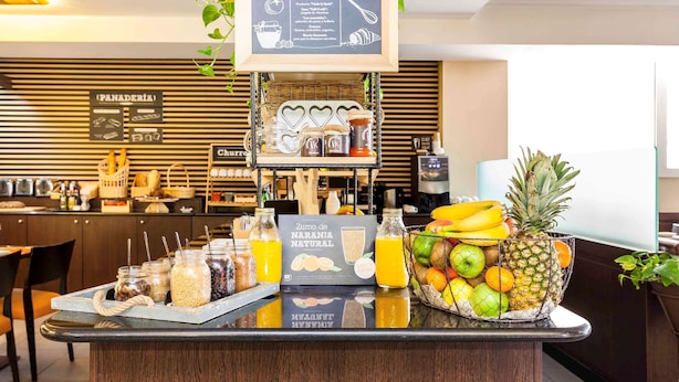 Una barra de desayuno con una pizarra de menú, frascos de condimentos, un cuenco de frutas y un dispensador de jugo.